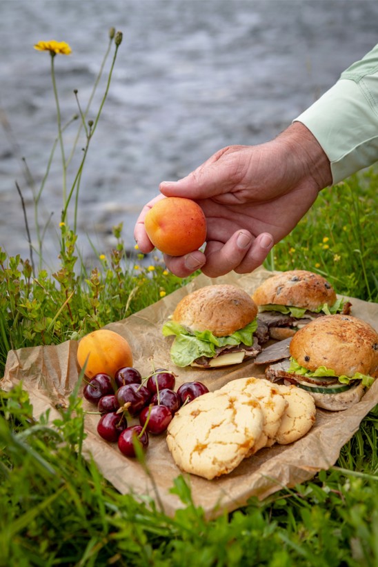 A plate of cherries, cookies, and sandwiches, on the group at rivers edge.